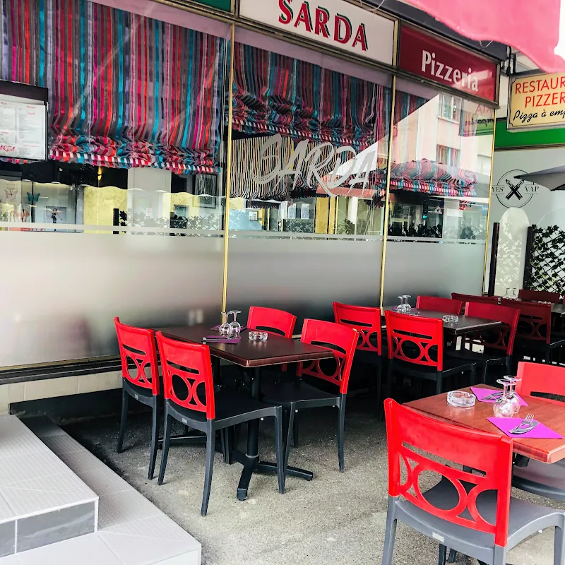 La terrasse de la Pizzéria Sarda : chaises rouges et stores rayés